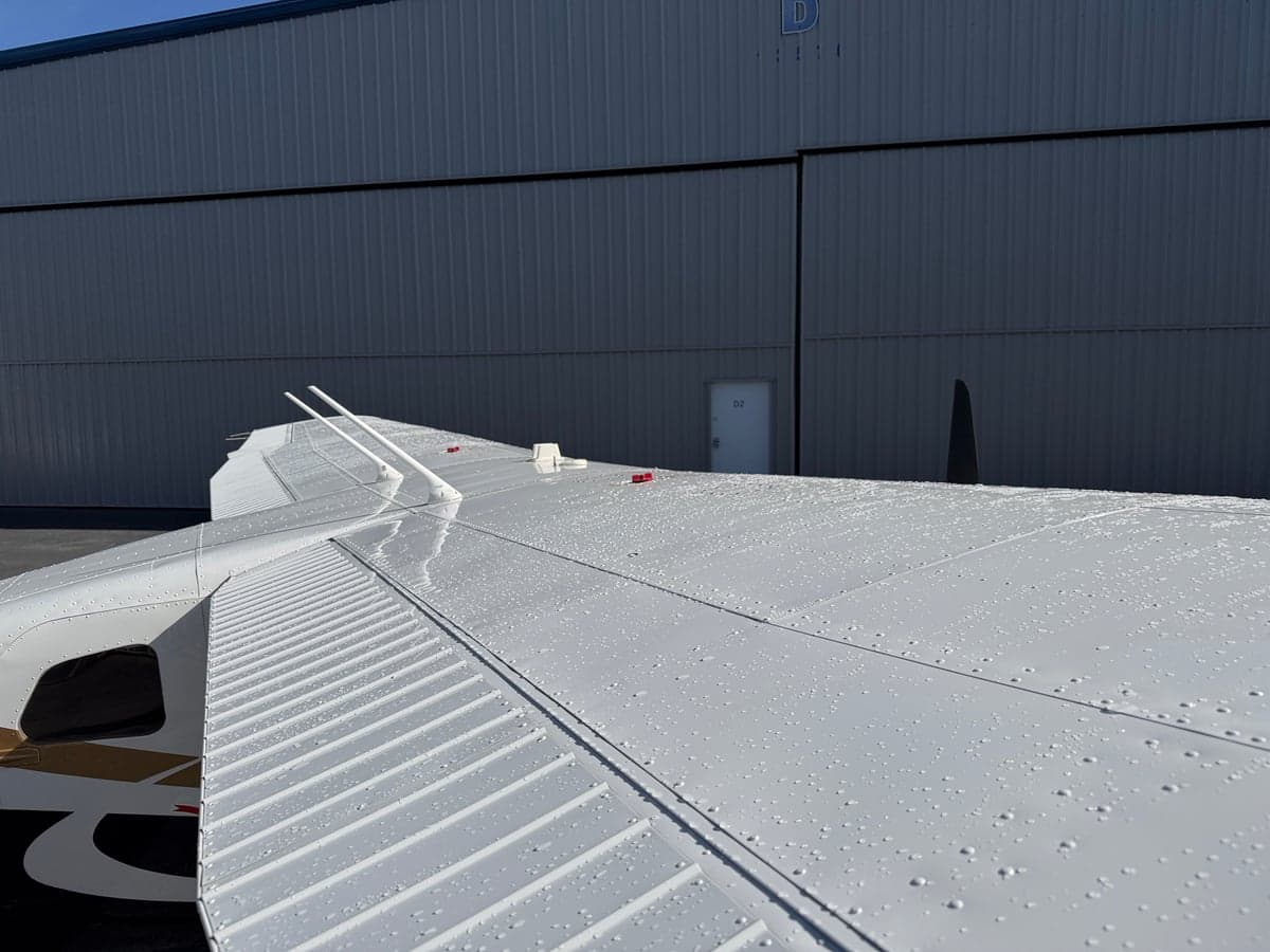 View of the aircraft wing with water droplets on a sunny day.