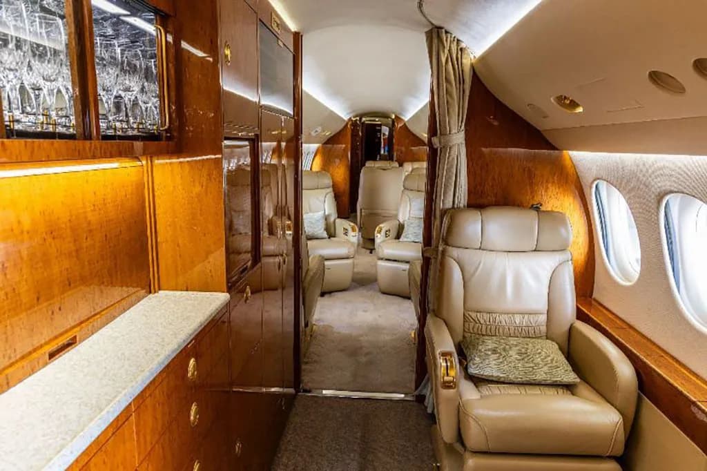 A view of the private jet's cabin showing a galley area with glassware and tan leather seats.