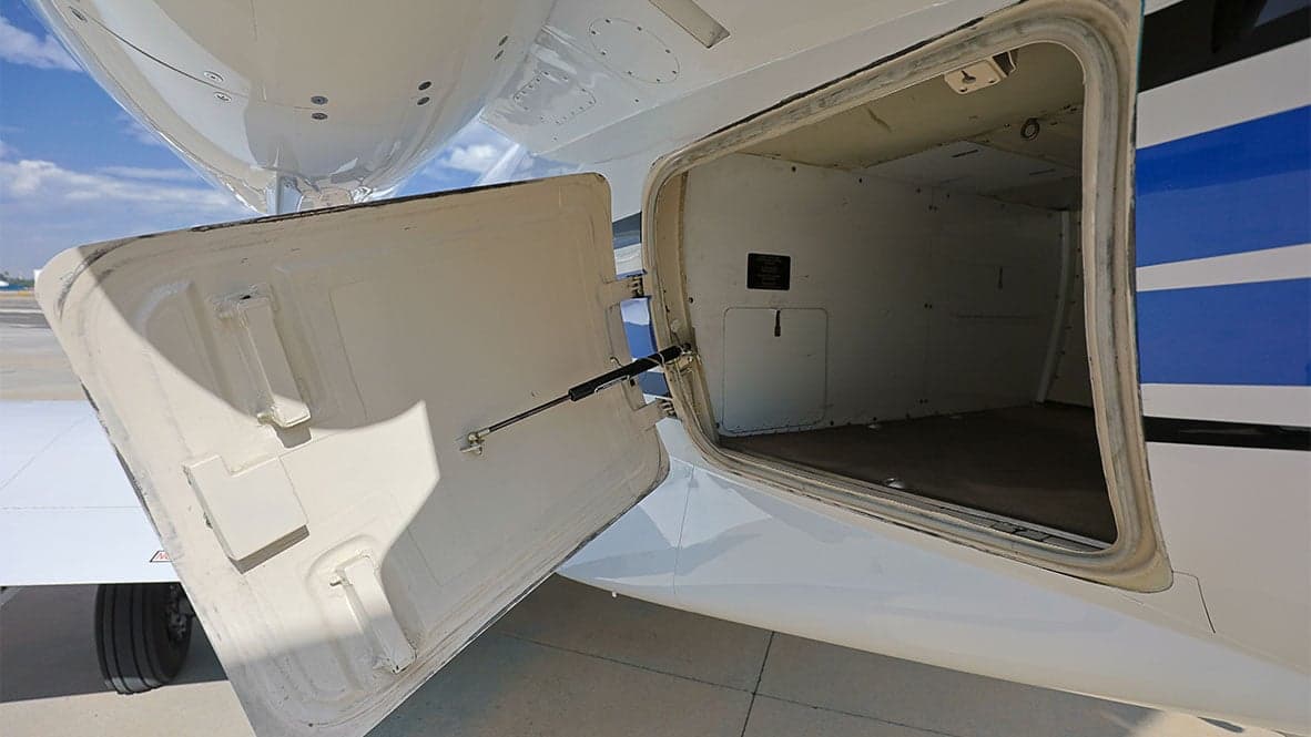 A close-up of the open baggage compartment door on a white and blue Cessna Citation CJ1 aircraft.