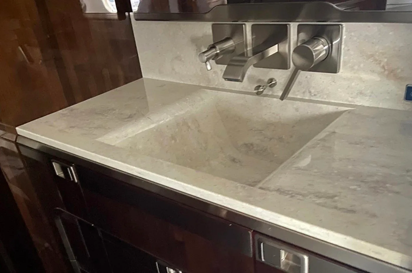 A modern white marble sink with a chrome faucet in the lavatory or galley of a private jet, surrounded by dark wood.