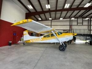 A Cessna 185 Skywagon, registration N185GS, is parked inside a hangar.