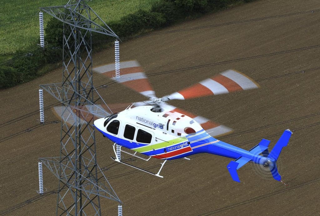 A National Grid helicopter flies near a power line tower.