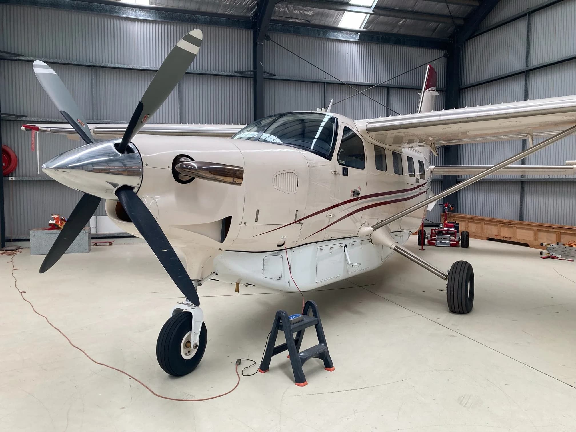 A beige Quest Kodiak 100 aircraft with red stripes, parked inside a hangar with its propeller visible.