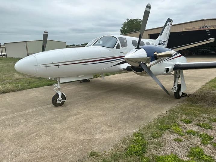 A white twin-engine propeller aircraft with dark red stripes, tail number N209C, parked on a tarmac.