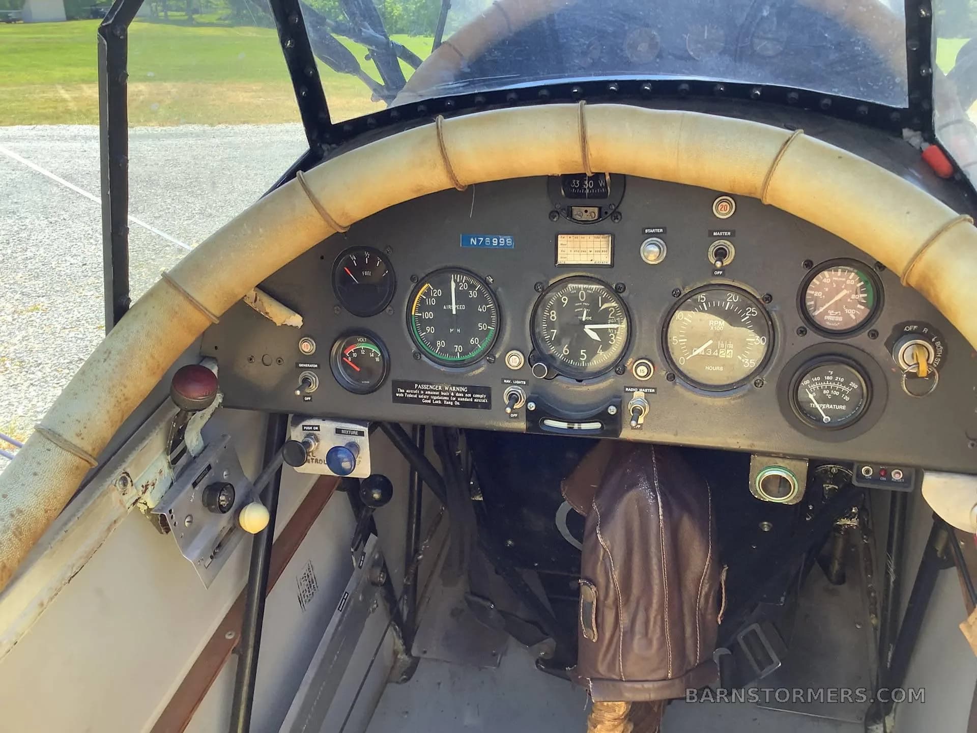 The cockpit of a biplane, showing the instrument panel with various gauges and a worn leather-wrapped control stick.