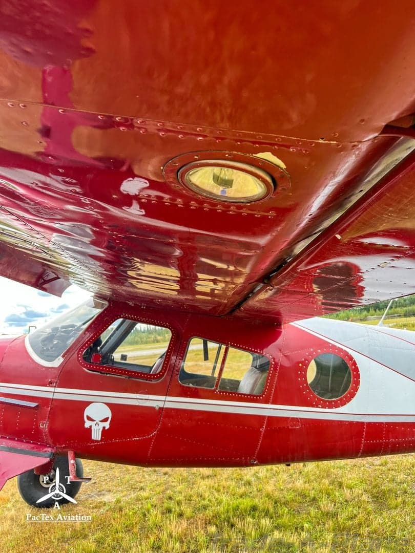 A close-up view of the red fuselage and underside of the wing of an aircraft, showing a landing light and a skull logo.