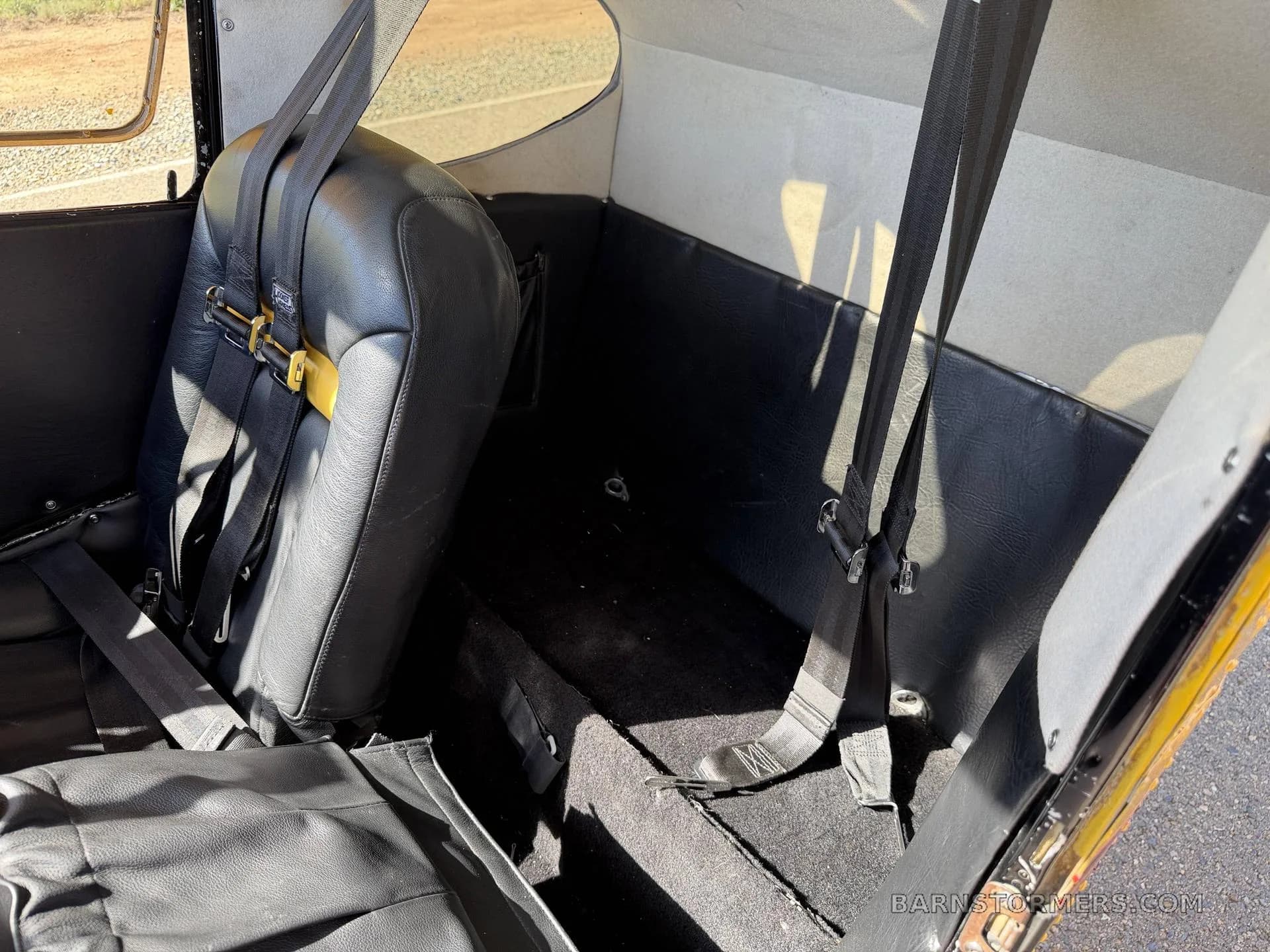 The rear interior of the aircraft features a single black leather seat with a seatbelt and a carpeted floor, looking towards the back.