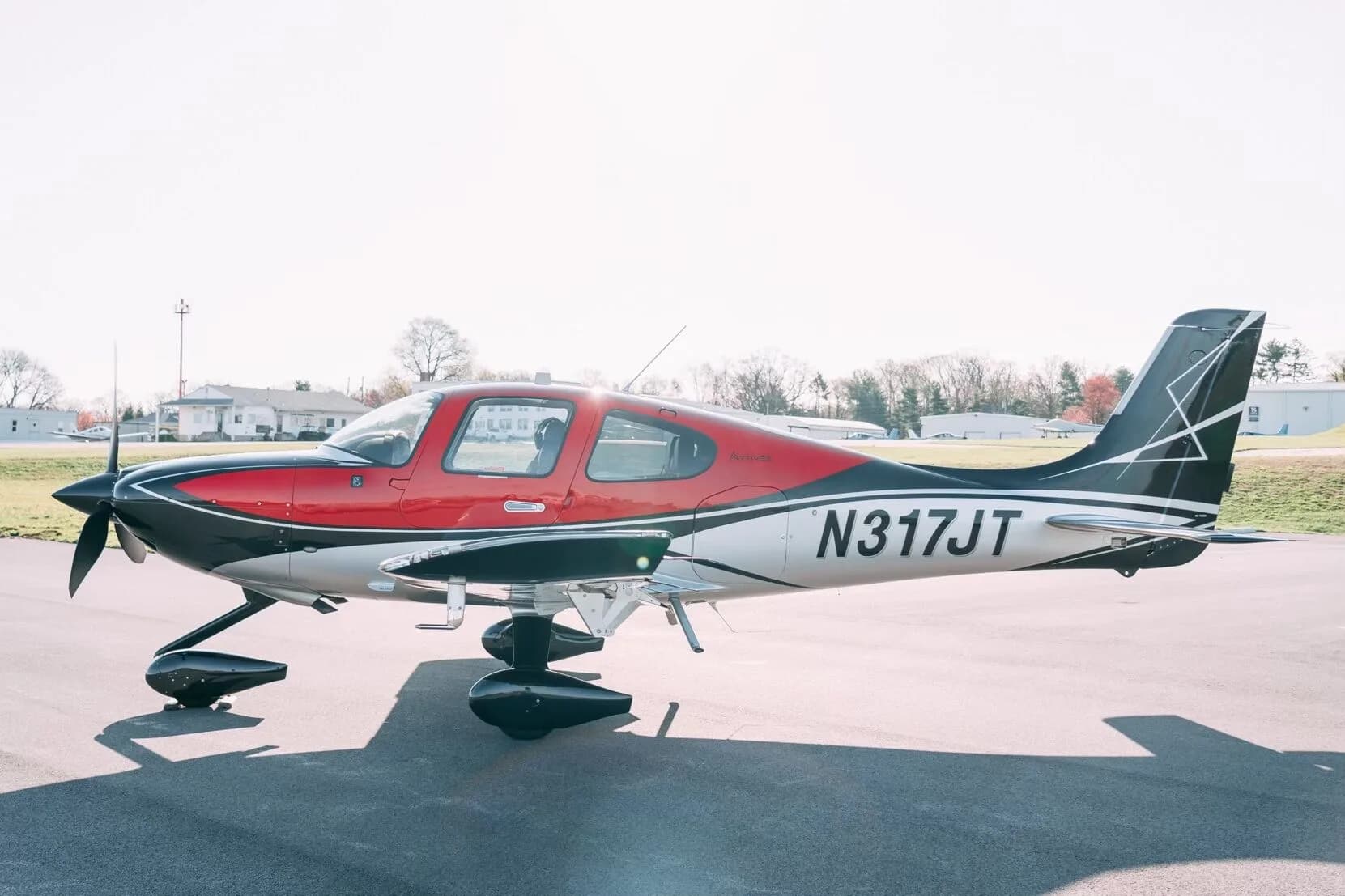 A red, black, and silver Cirrus SR22T aircraft (N317JT) parked on an asphalt tarmac under bright sunlight.