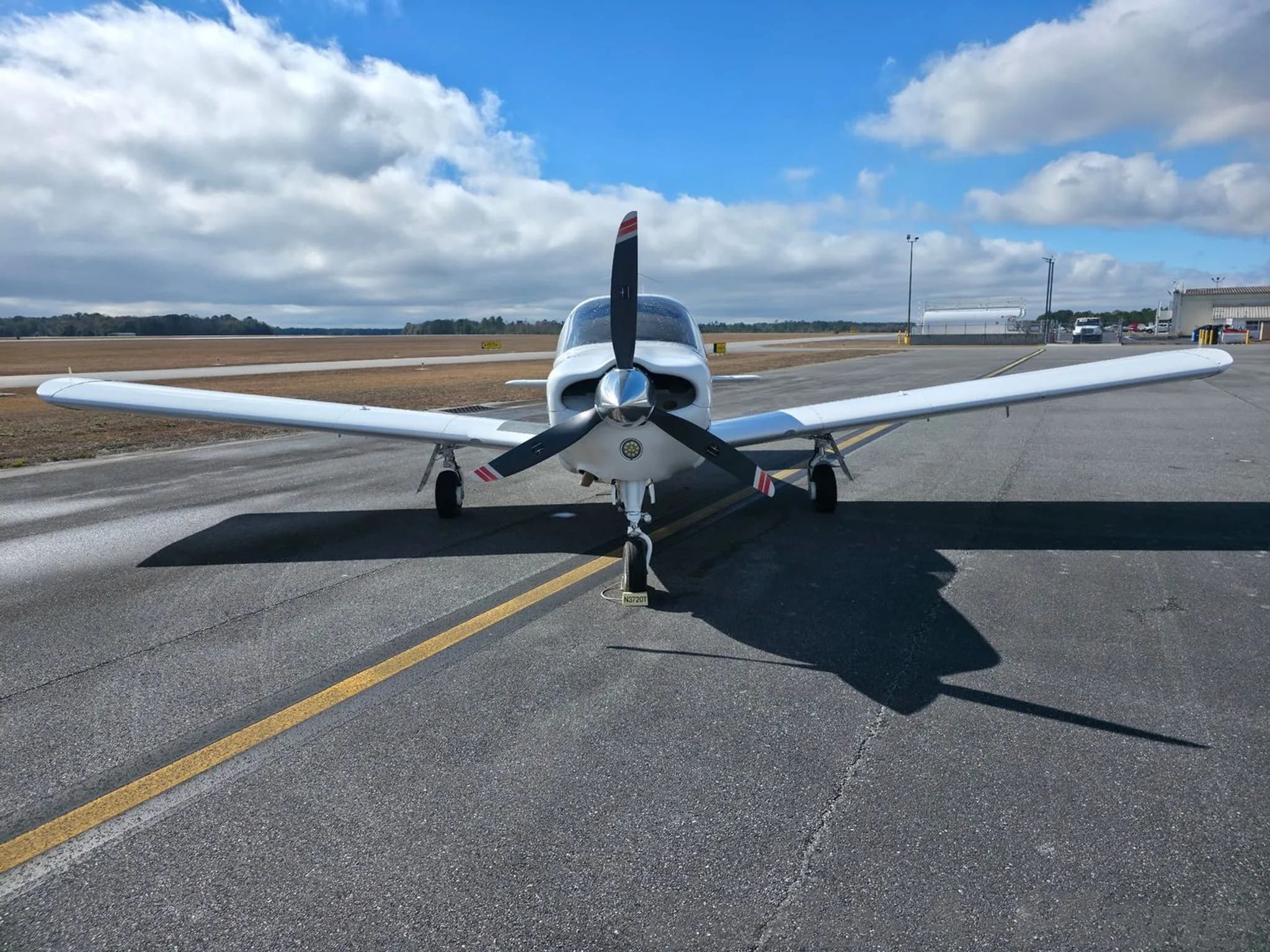 A head-on view of the white Piper Arrow N3720T, showing the propeller and wings, parked on an airfield.