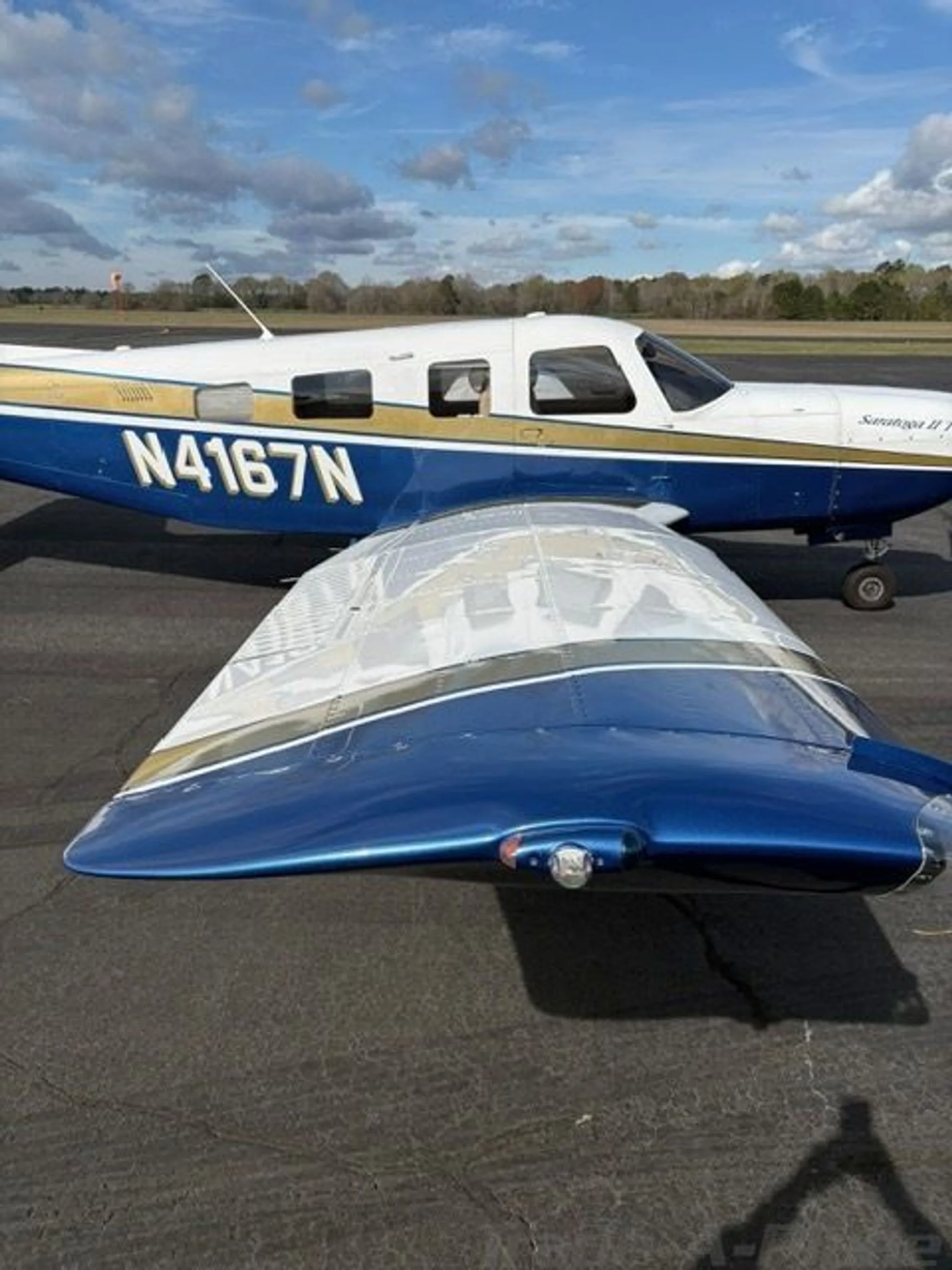 A close-up view of the left wing and fuselage of the Piper Saratoga II TC, N4167N, showing its white, blue, and gold paint scheme.