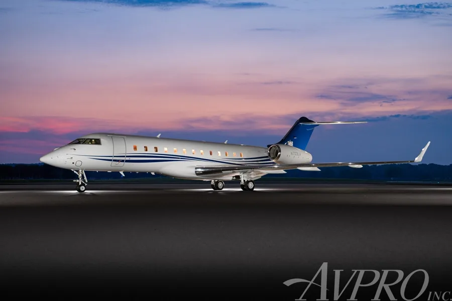 A Bombardier Global 6000 business jet with blue and white livery on a tarmac at dusk.