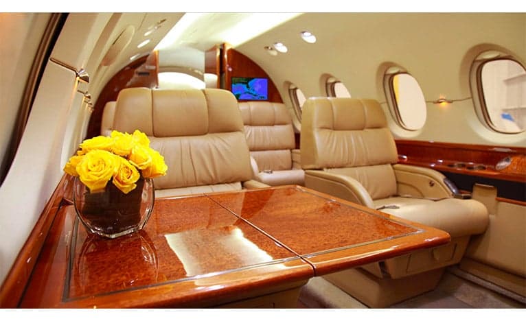 The interior of a Hawker jet with leather seats, a wooden table, and a vase of yellow roses.