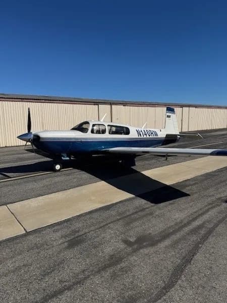 A white and blue single-engine propeller aircraft, N14DRM, parked on an asphalt tarmac in front of a hangar under a clear blue sky.