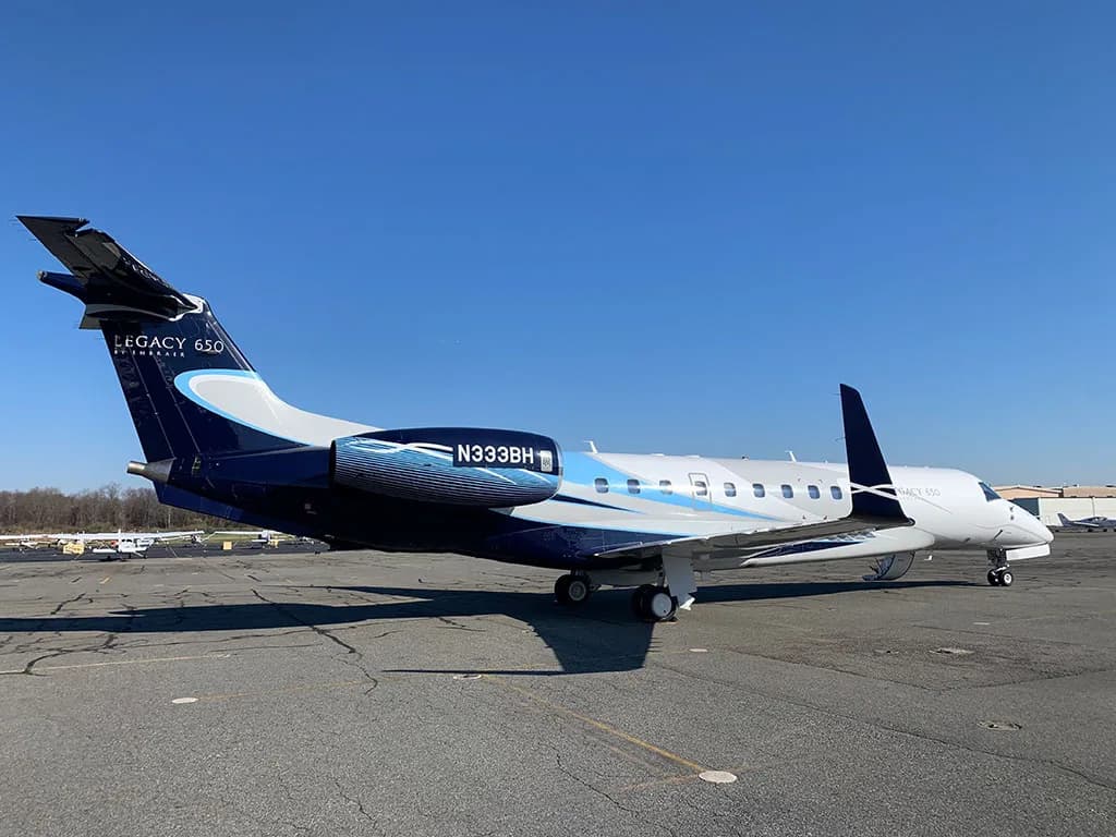 A side view of the Embraer Legacy 650 (N333BH) with its distinctive blue and white livery on an airport tarmac.