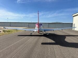 Rear view of a Cirrus SR22T aircraft on a tarmac with a hangar in the background.