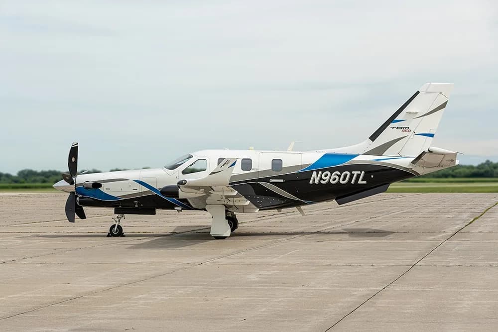 A TBM 960 turboprop aircraft, registration N960TL, parked on an airfield with a white, blue, and black paint scheme.