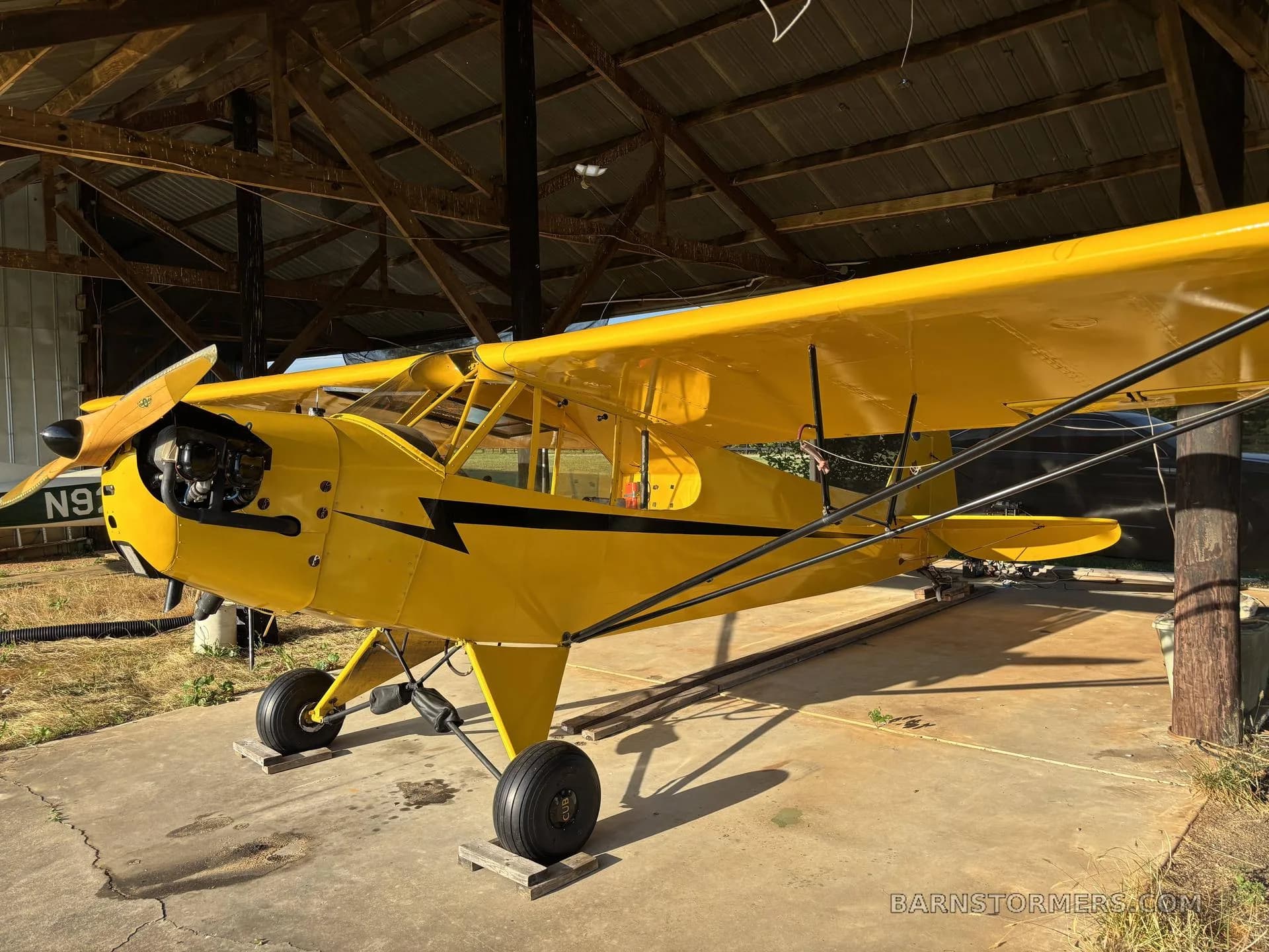A bright yellow vintage aircraft with a black lightning bolt stripe, parked inside a rustic wooden hangar.