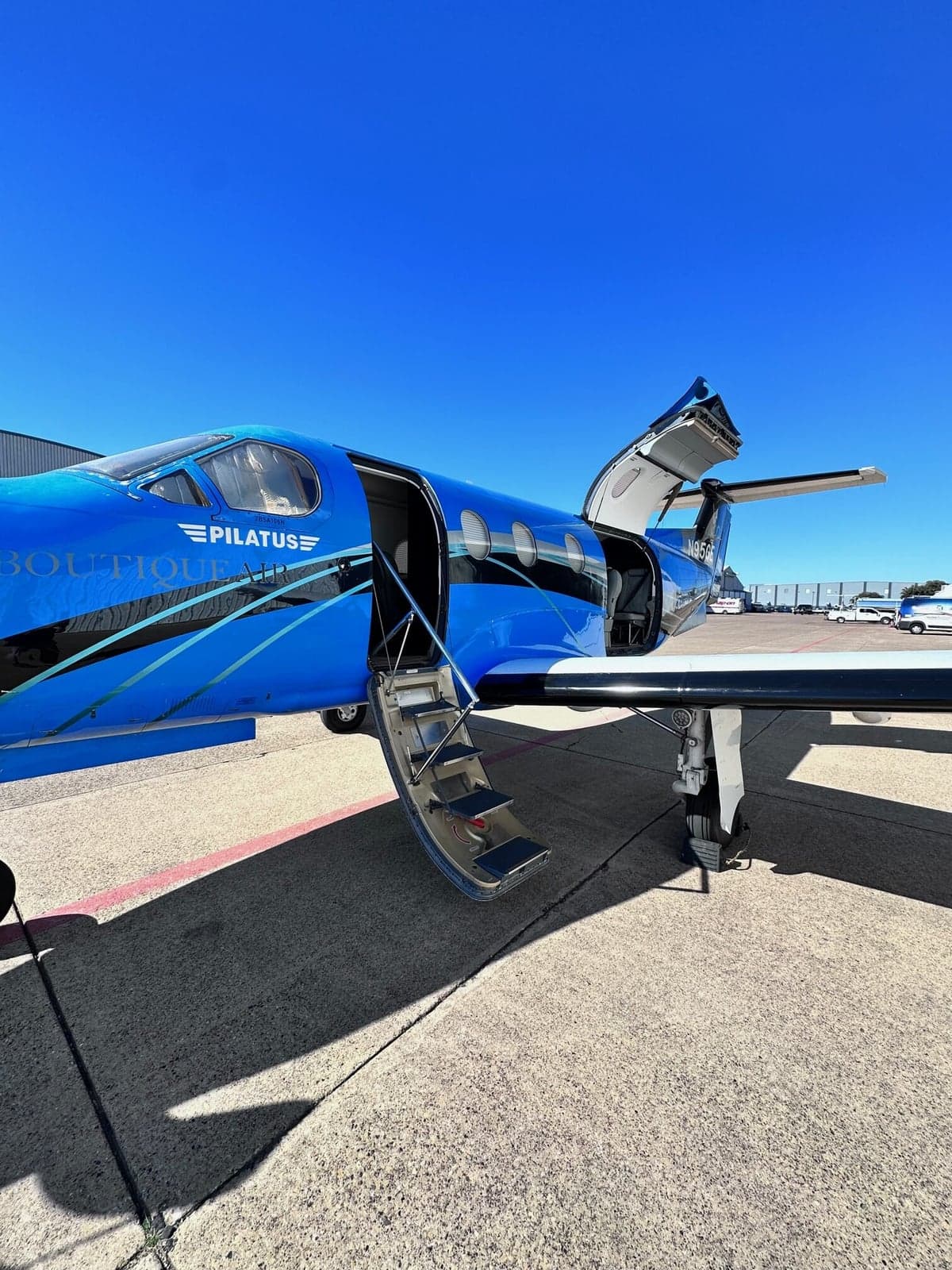 A blue Pilatus PC-12 aircraft with the door open and airstair extended on the ramp.