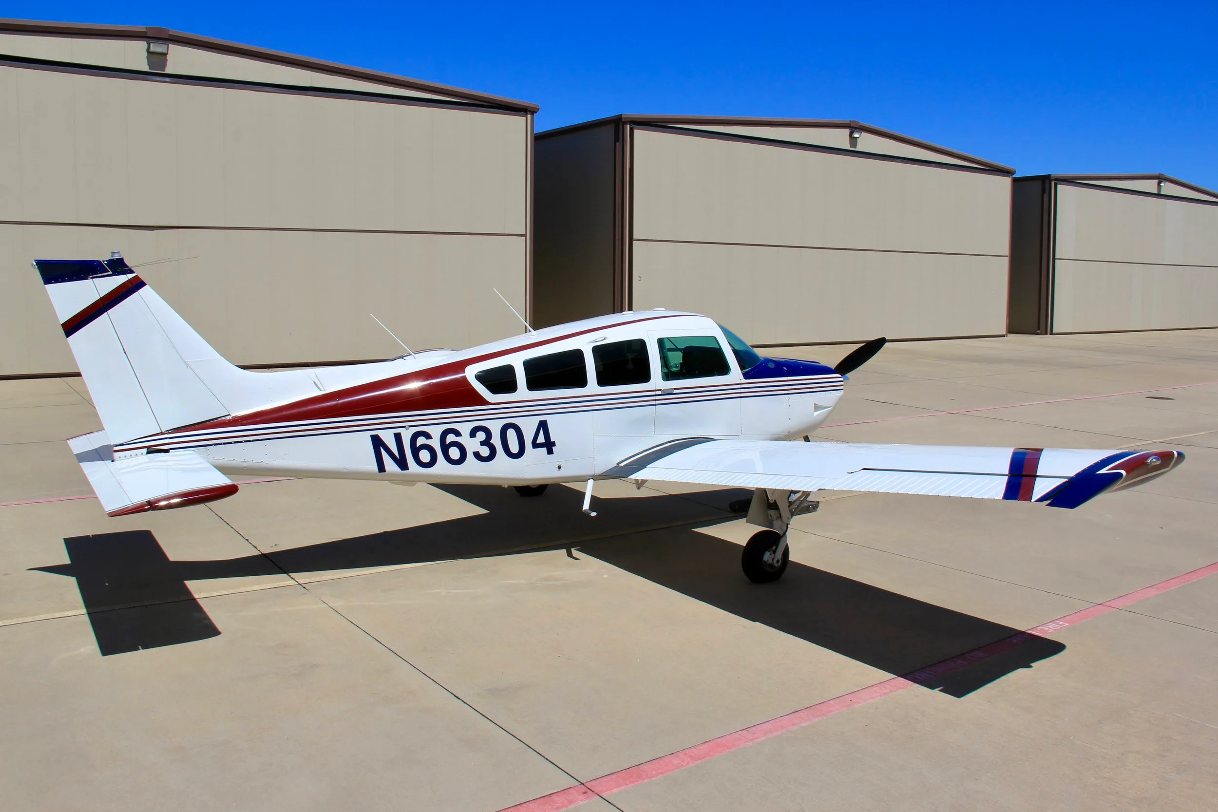 A three-quarter rear view of the white, blue, and red single-engine aircraft (N66304) parked on an tarmac.