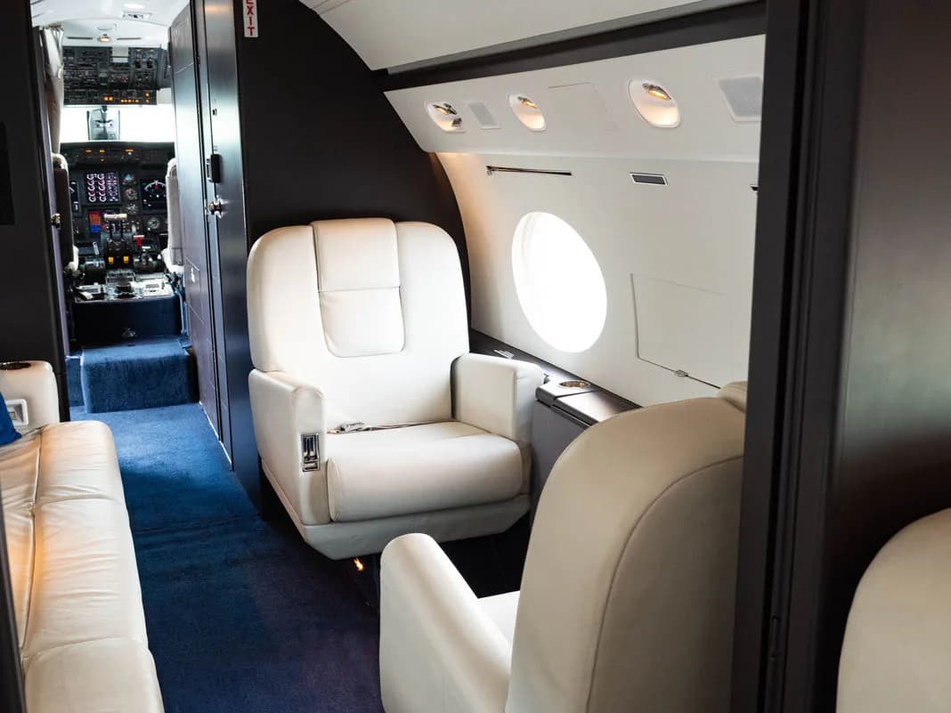 View of the aircraft interior with white leather seats and blue carpet.