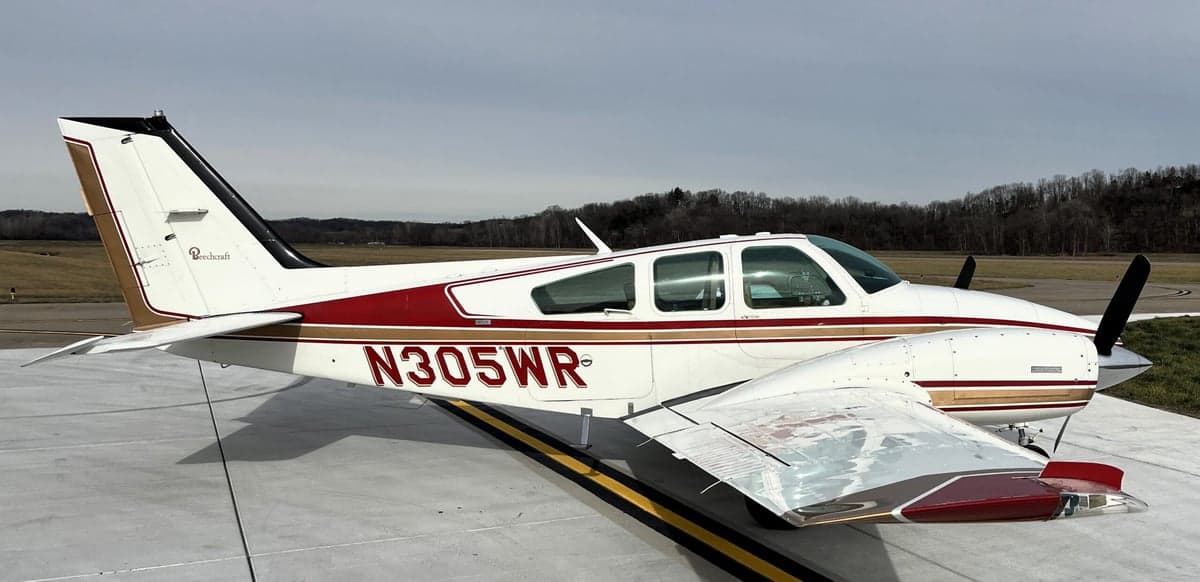 A Beechcraft Bonanza aircraft with a white and red paint scheme is parked on the tarmac.