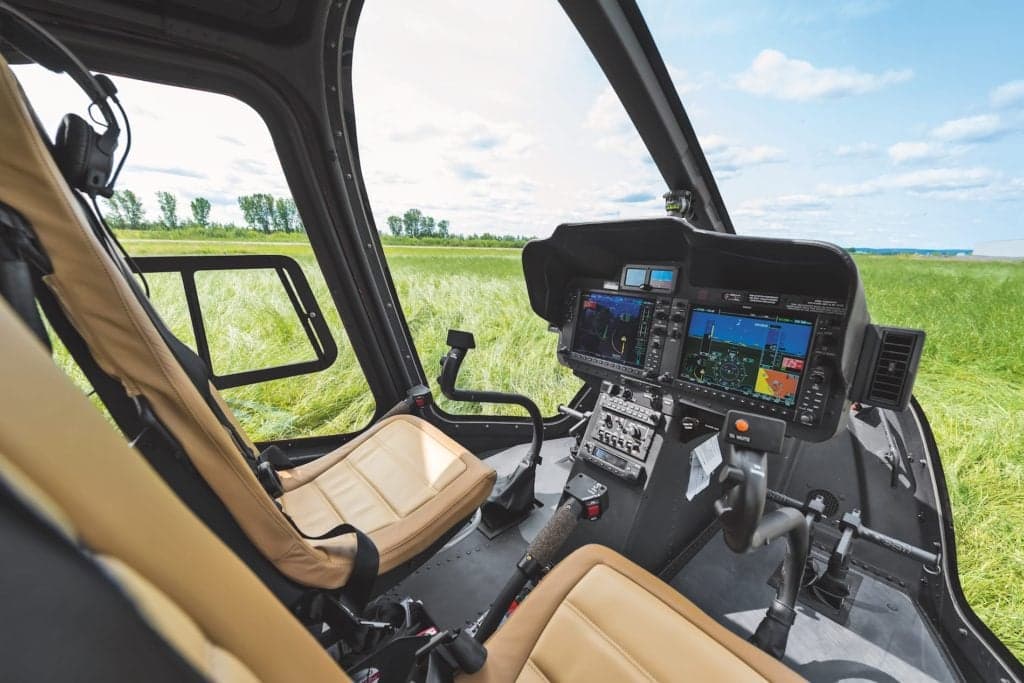 The cockpit of a helicopter with tan seats and modern avionics.
