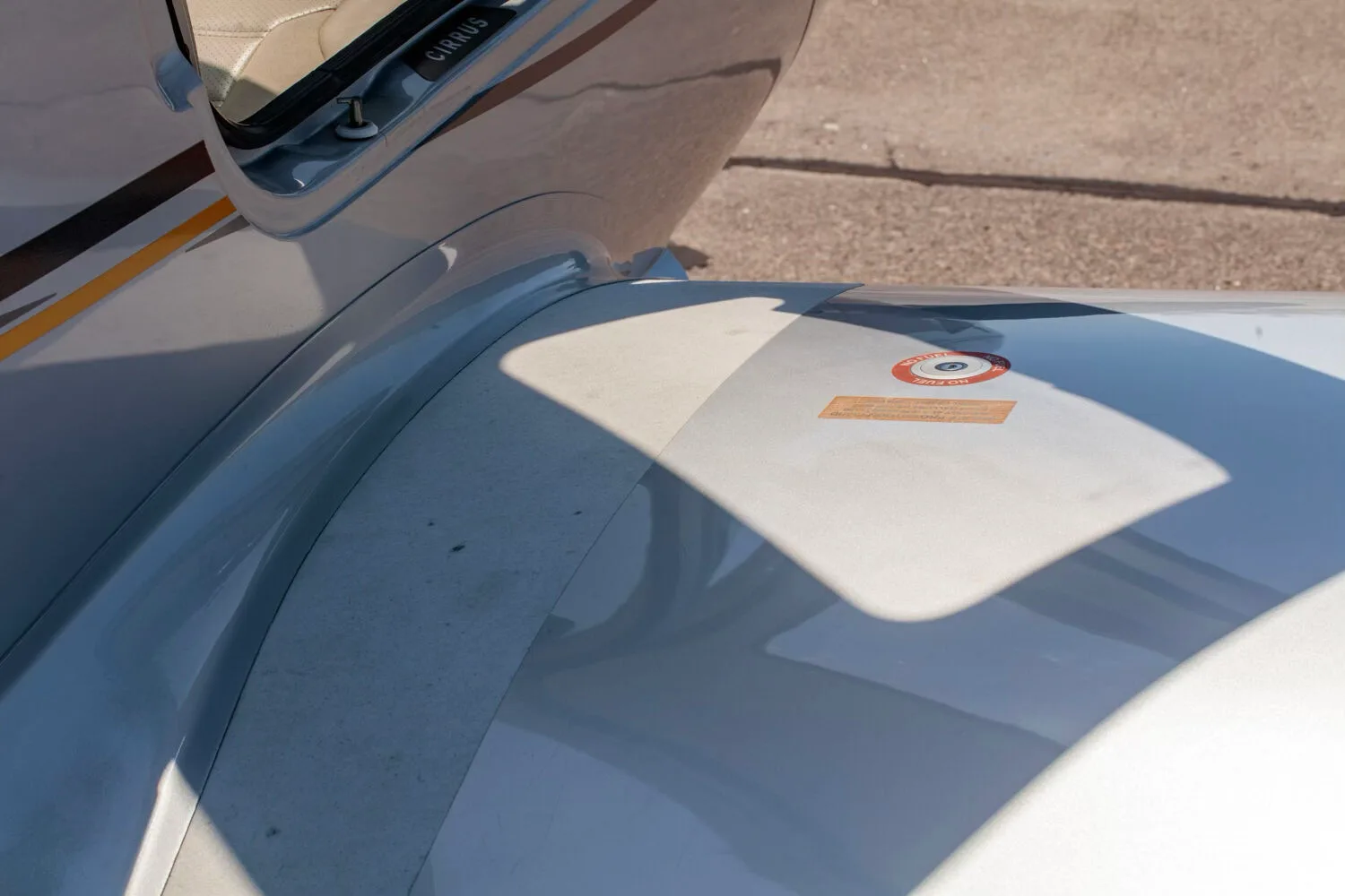 A close-up view of the wing root and fuselage of the silver Cirrus SR22T aircraft, showing a warning label.