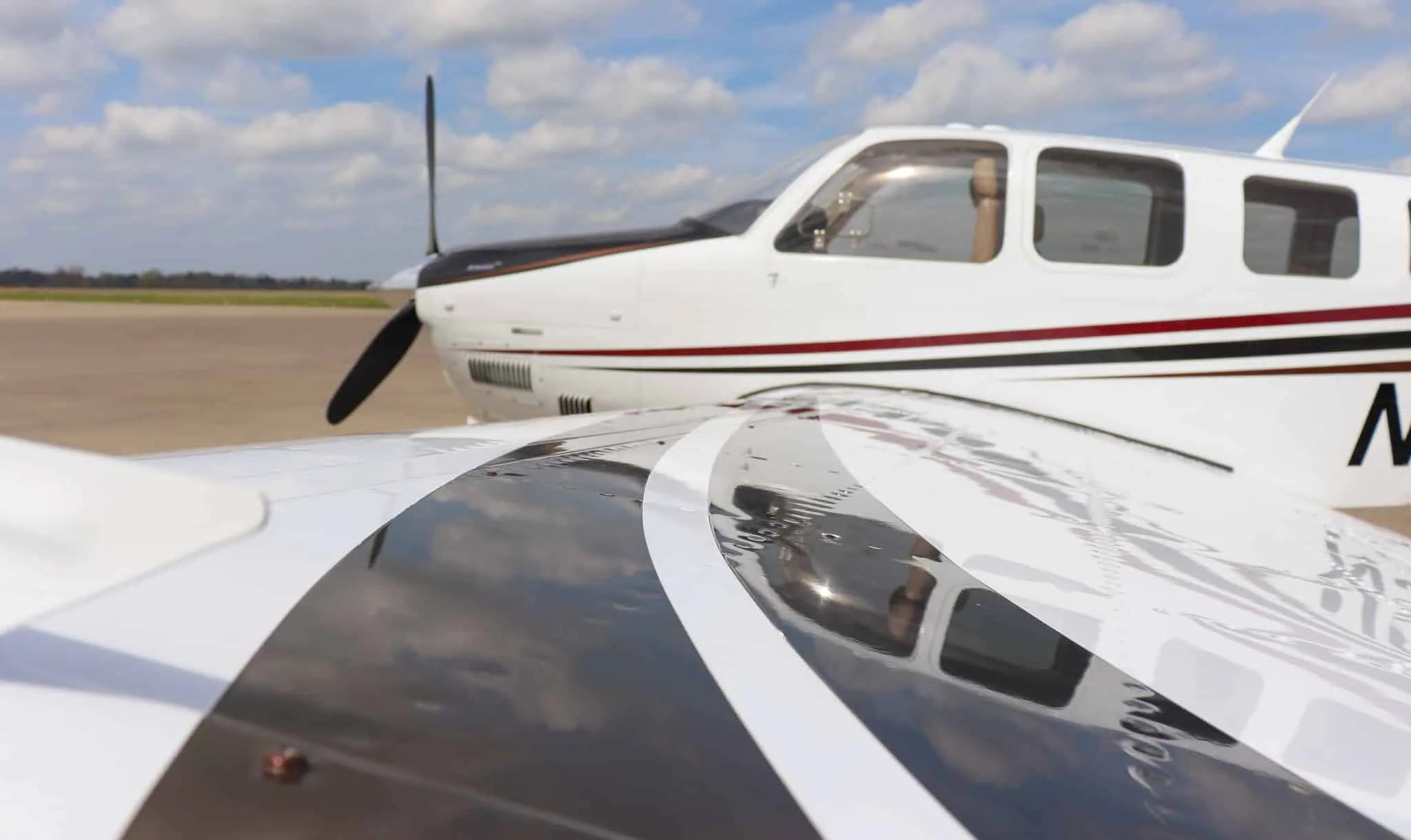 A close-up view of the wing and fuselage of the aircraft, showing reflections and part of the propeller.