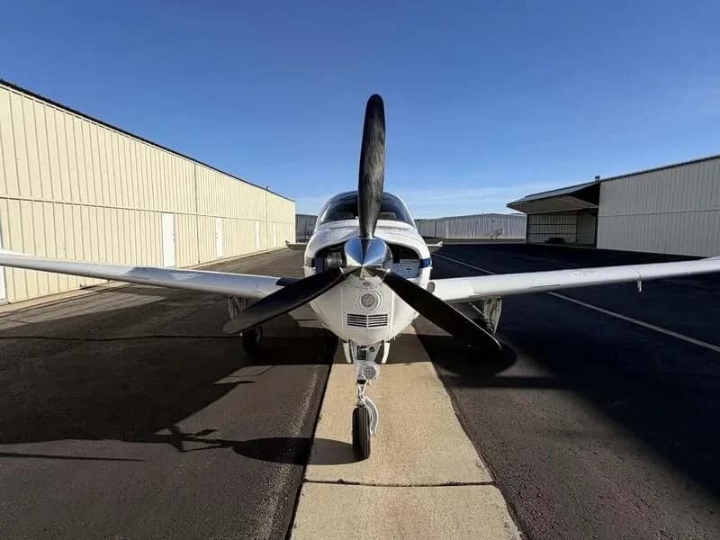 A head-on view of the white Beechcraft Bonanza N455JR, showing its propeller and landing gear.