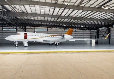 A white and gold private jet parked inside a hangar with the door open.
