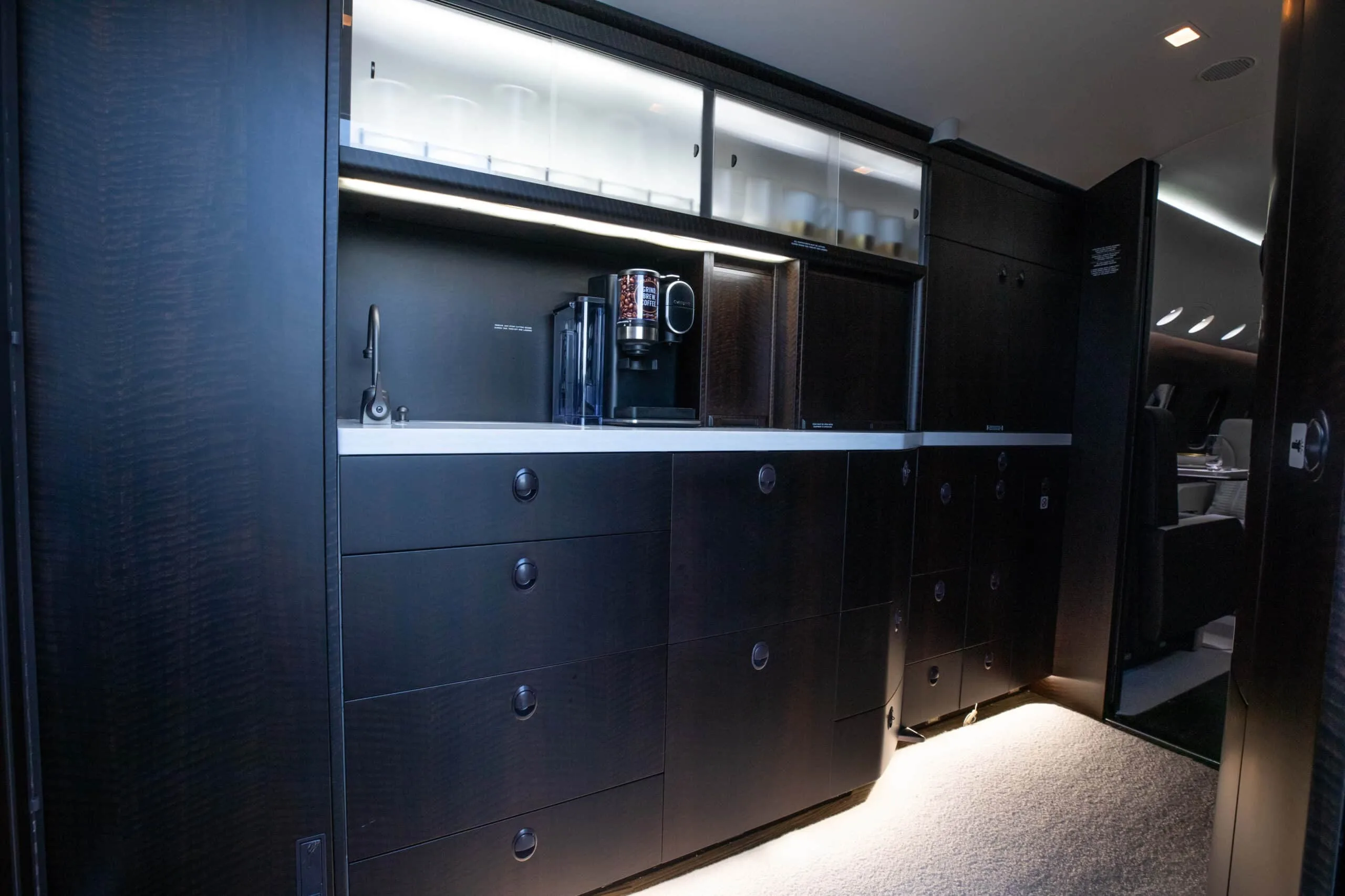 The aircraft's galley area with dark wood cabinetry, a coffee machine, and a sink.