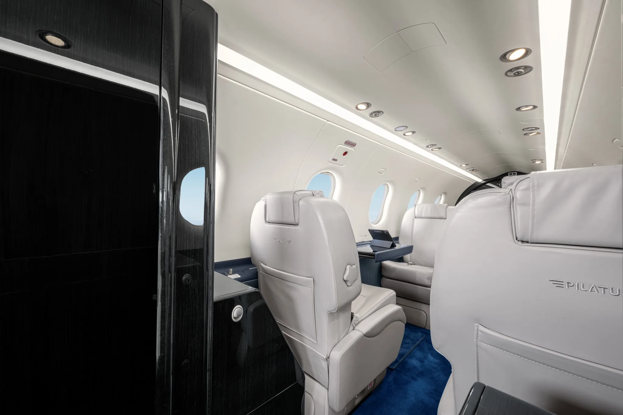 A side view of the aircraft's cabin interior, highlighting light grey seats, a dark blue side panel, and a black cabinet.