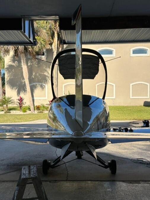 Rear view of an aircraft with an open canopy in front of a house.