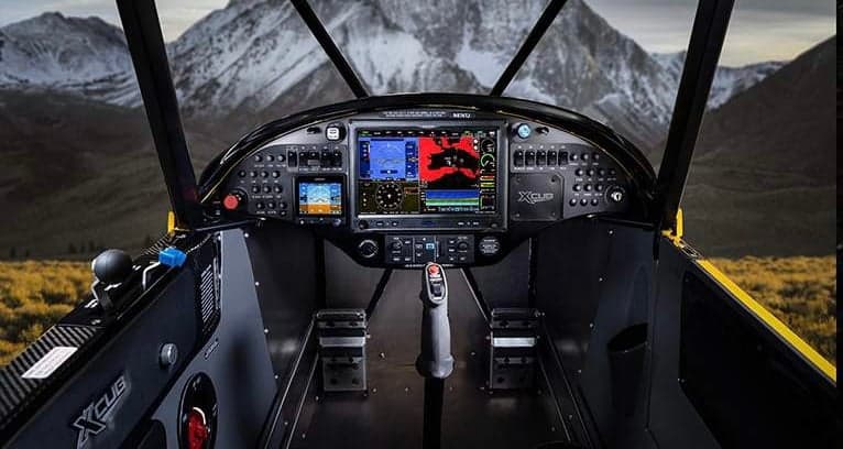 The cockpit of an XCub aircraft with a mountain view in the background.