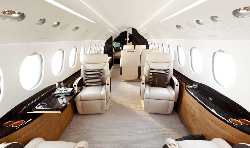 Interior view of a Falcon 8X cabin with leather seats and wood trim.