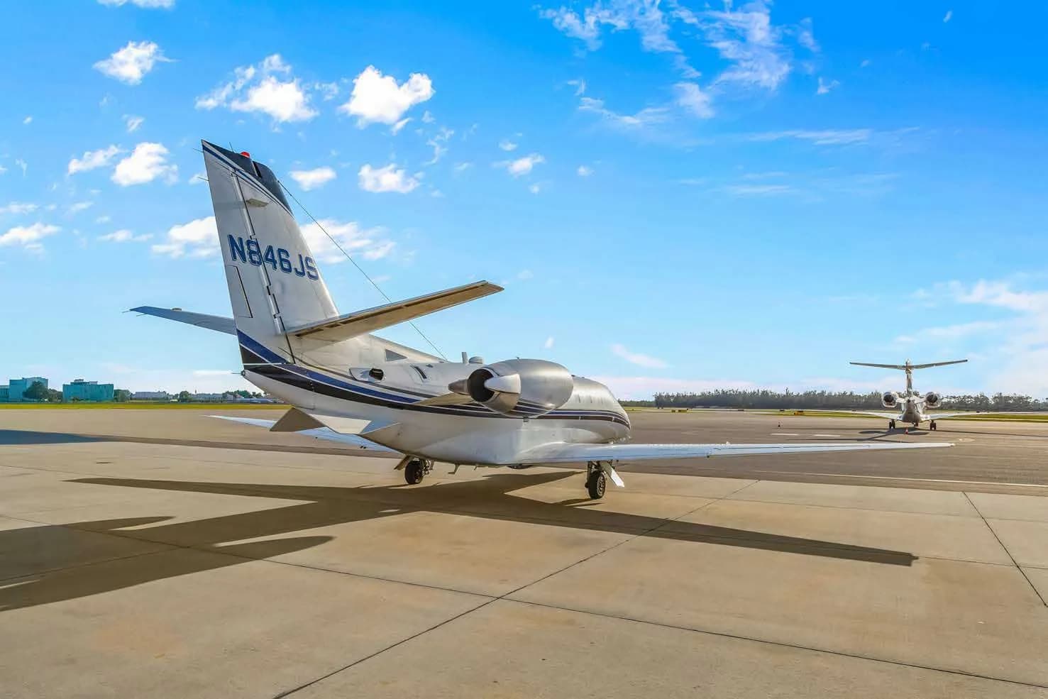 A rear three-quarter view of a white Cessna Citation business jet, N846JS, parked on an airport tarmac with another jet in the background.