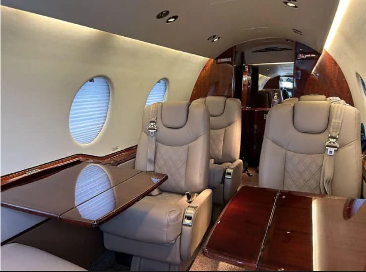 Aircraft cabin with tan leather seats and fold-out tables.