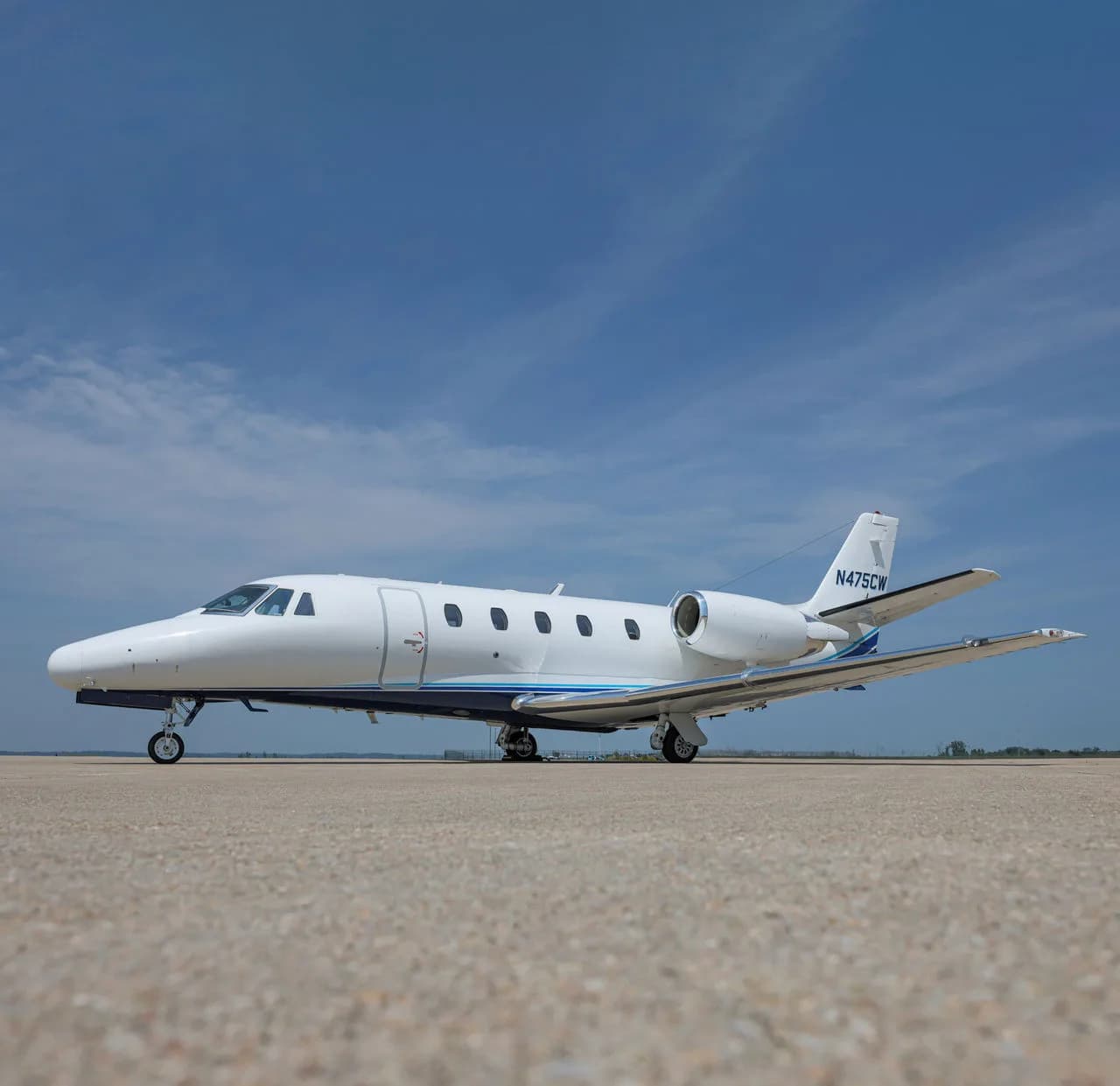 A white jet with blue accents parked on the tarmac under a blue sky.