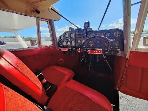 View of the aircraft's red seats and instrument panel from inside the cockpit.