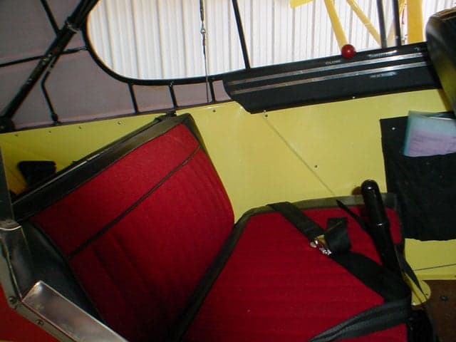 The front interior cabin of the Piper Super Cub aircraft, showing red seats and yellow side panels.