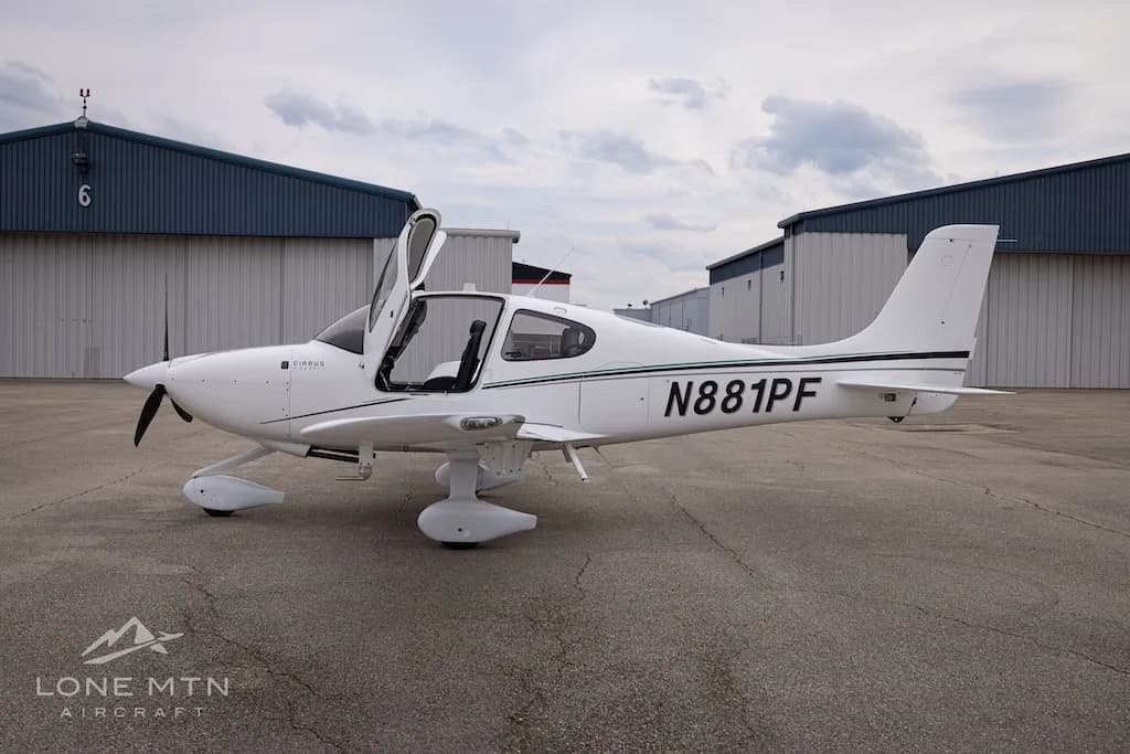 A white Cirrus SR22 aircraft with N881PF registration and green accent stripes, parked on an asphalt ramp with its doors open.