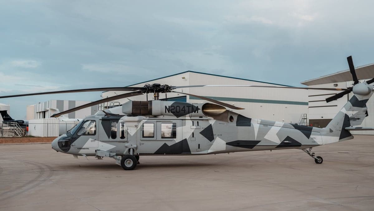 Side view of a Sikorsky S-70i helicopter with a gray camouflage paint scheme on the tarmac.