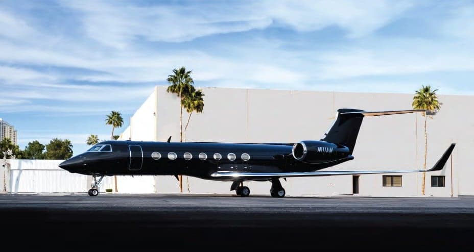 A black Gulfstream G650 is parked in front of a building with palm trees.