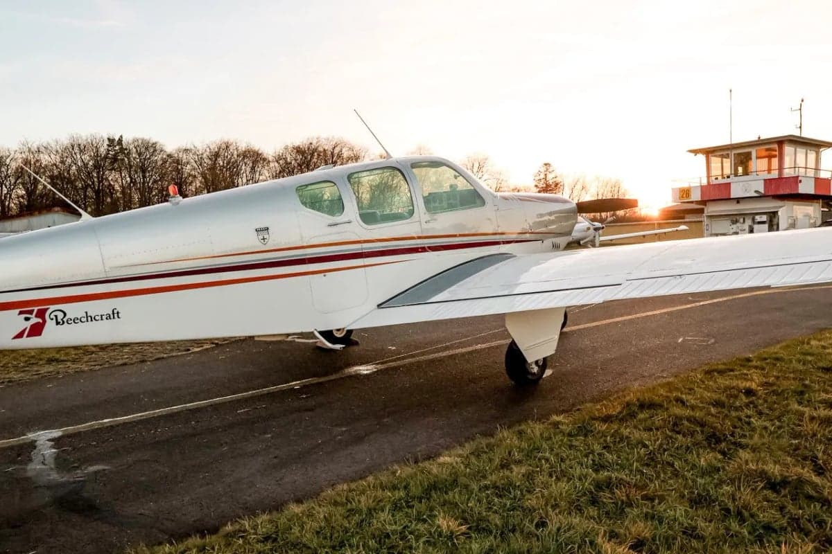 Beechcraft Bonanza N8918M parked on the runway near an airport tower.
