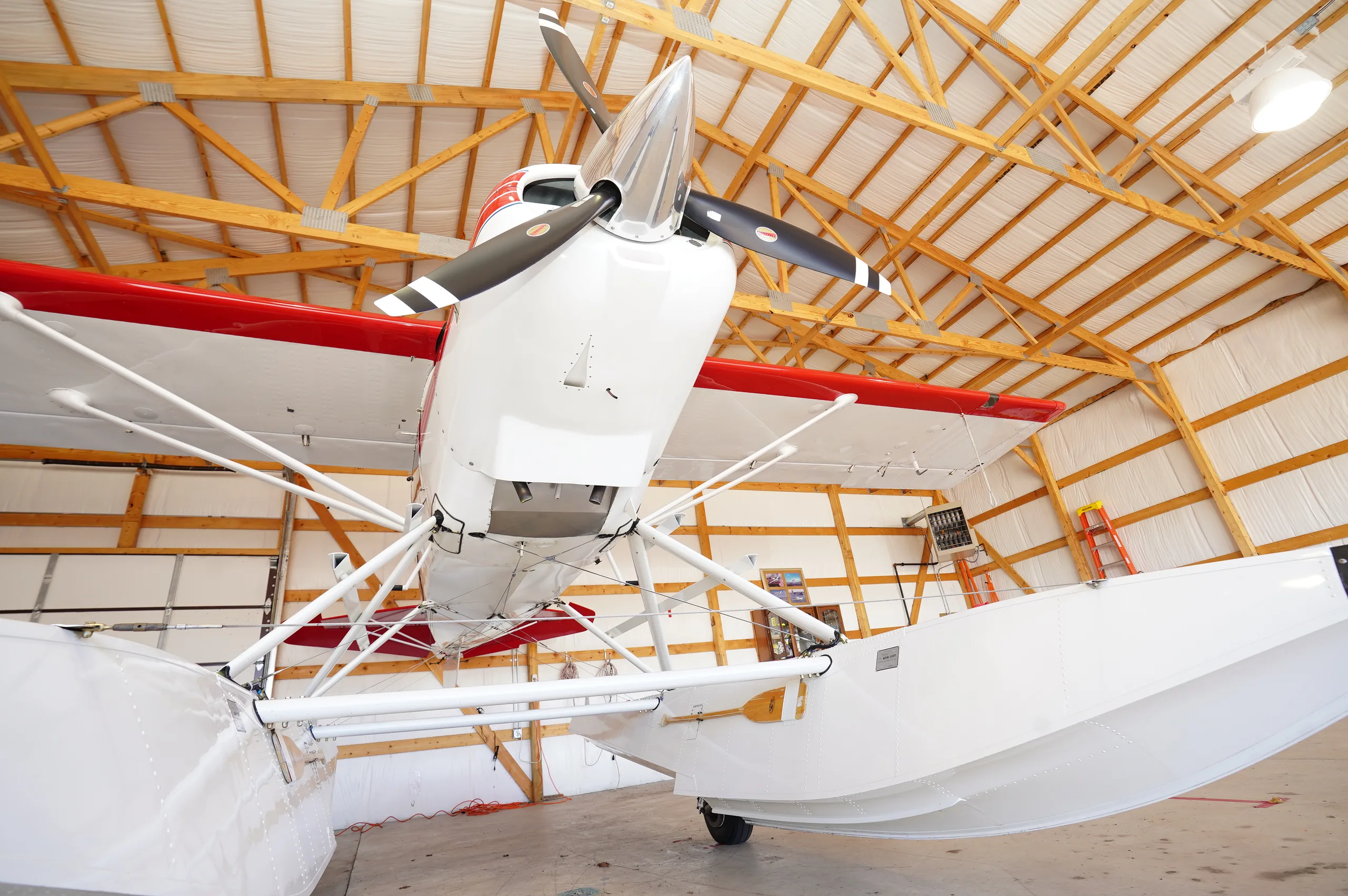 An upward view of the white Maule floatplane's propeller and floats inside a hangar.