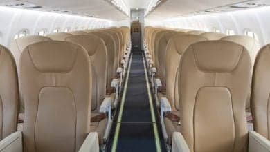 Interior view of an aircraft cabin with rows of tan leather seats.