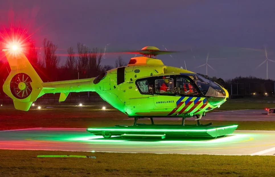 A bright green ambulance helicopter with red and blue stripes on its side, illuminated at night on a helipad.