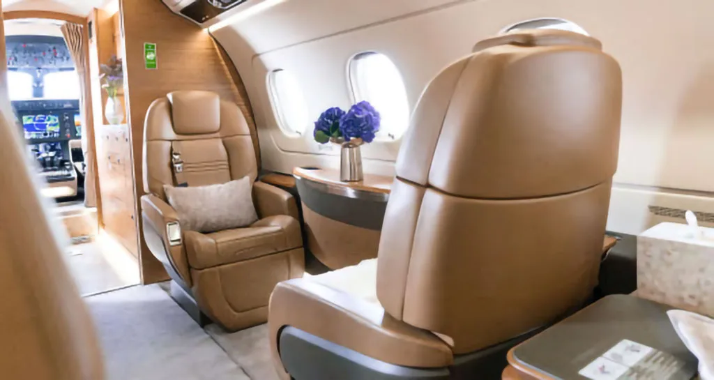 The interior of a business jet cabin with tan leather seats and a glimpse of the cockpit in the background.