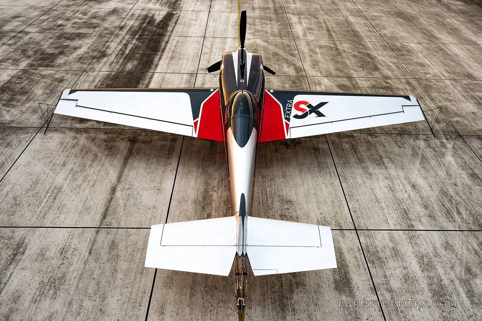 An overhead rear view of a red, black, and silver Extra 330SC aerobatic aircraft parked on a concrete runway.