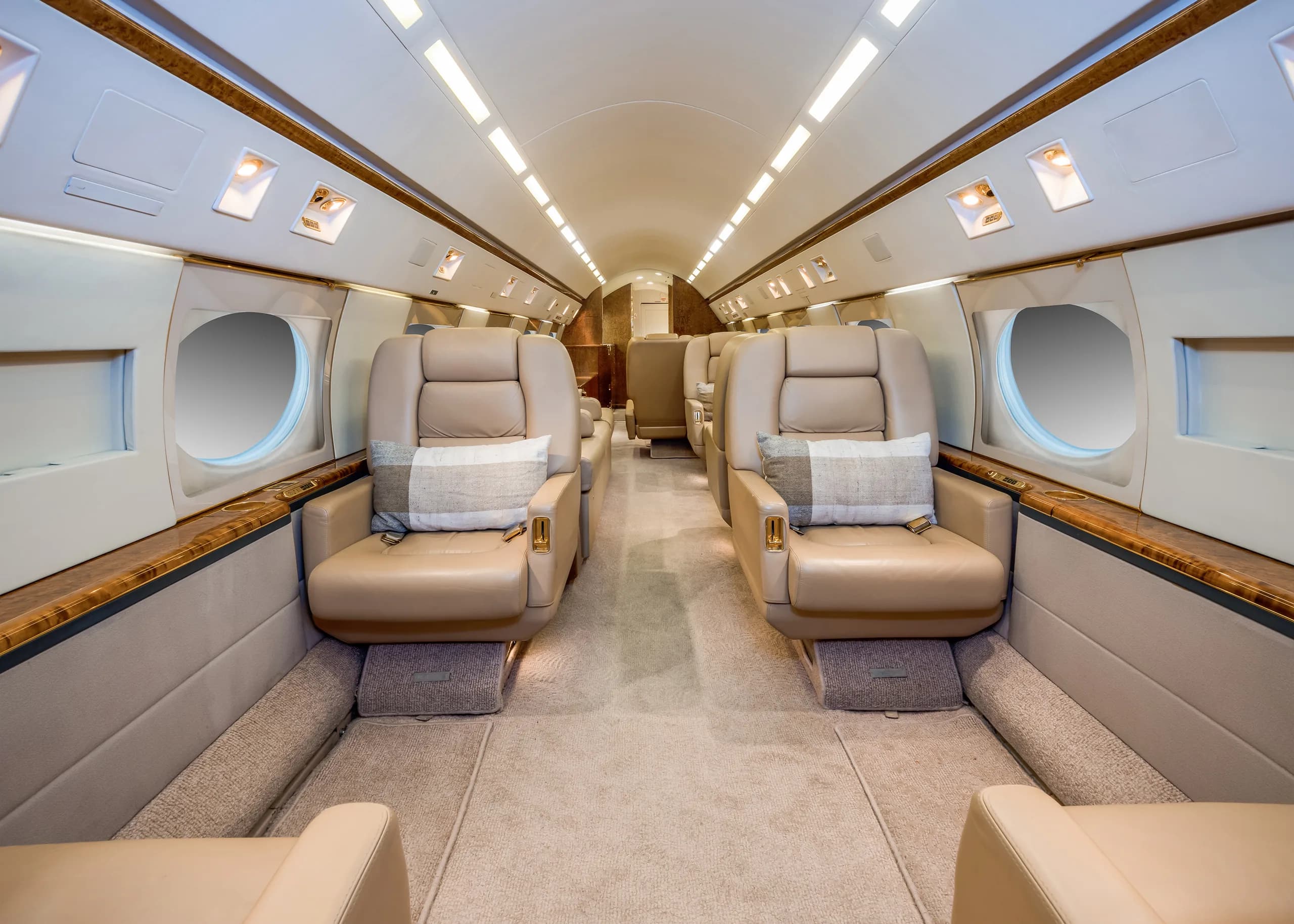 A luxurious aircraft cabin with two rows of beige leather seats facing each other, each with a plaid pillow.